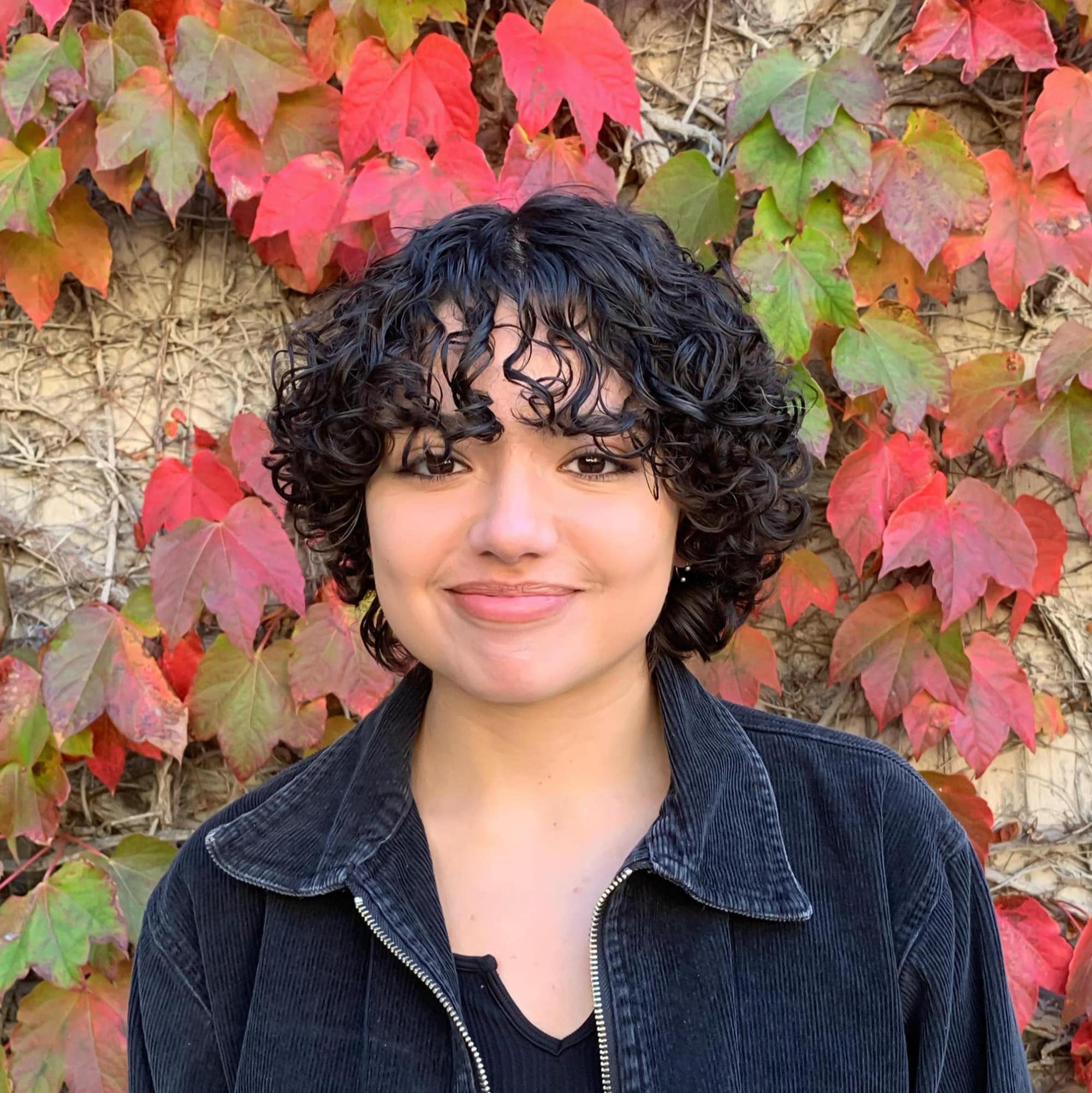 Rosario Ortiz standing in front of a red and green ivy wall.